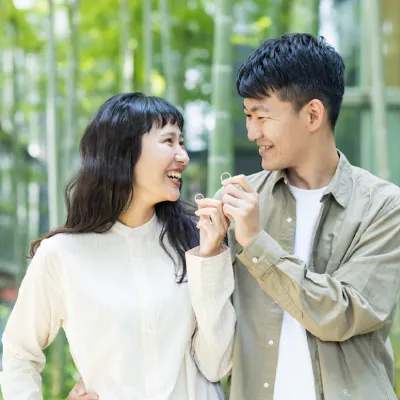 竹林を背景に、男女が小さな輪を手に持ち、笑顔で見つめ合っている。