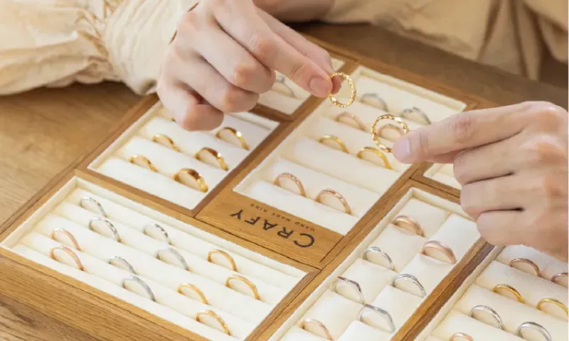 木製のトレーに並べられた様々なデザインの指輪を、手に取って選んでいる様子。