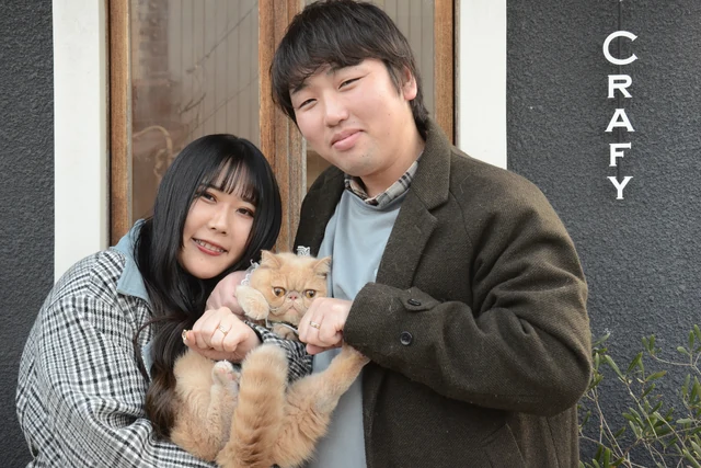 猫を抱いて店舗の前で記念撮影するおふたり